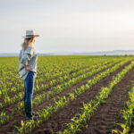 Satisfied female farmer is looking at corn field in cultivated l